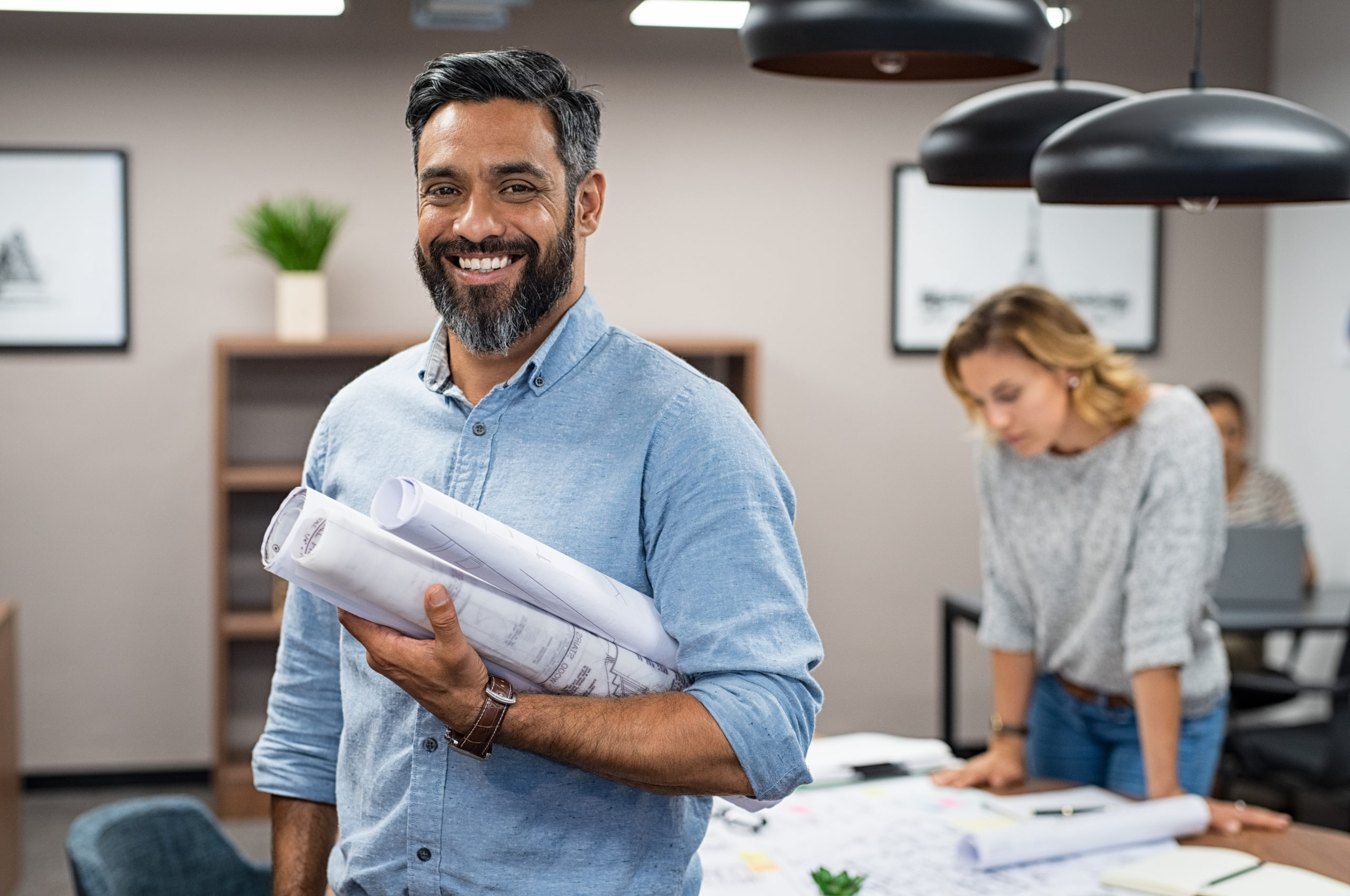 A multiethnic architect in a creative office, holding blueprints