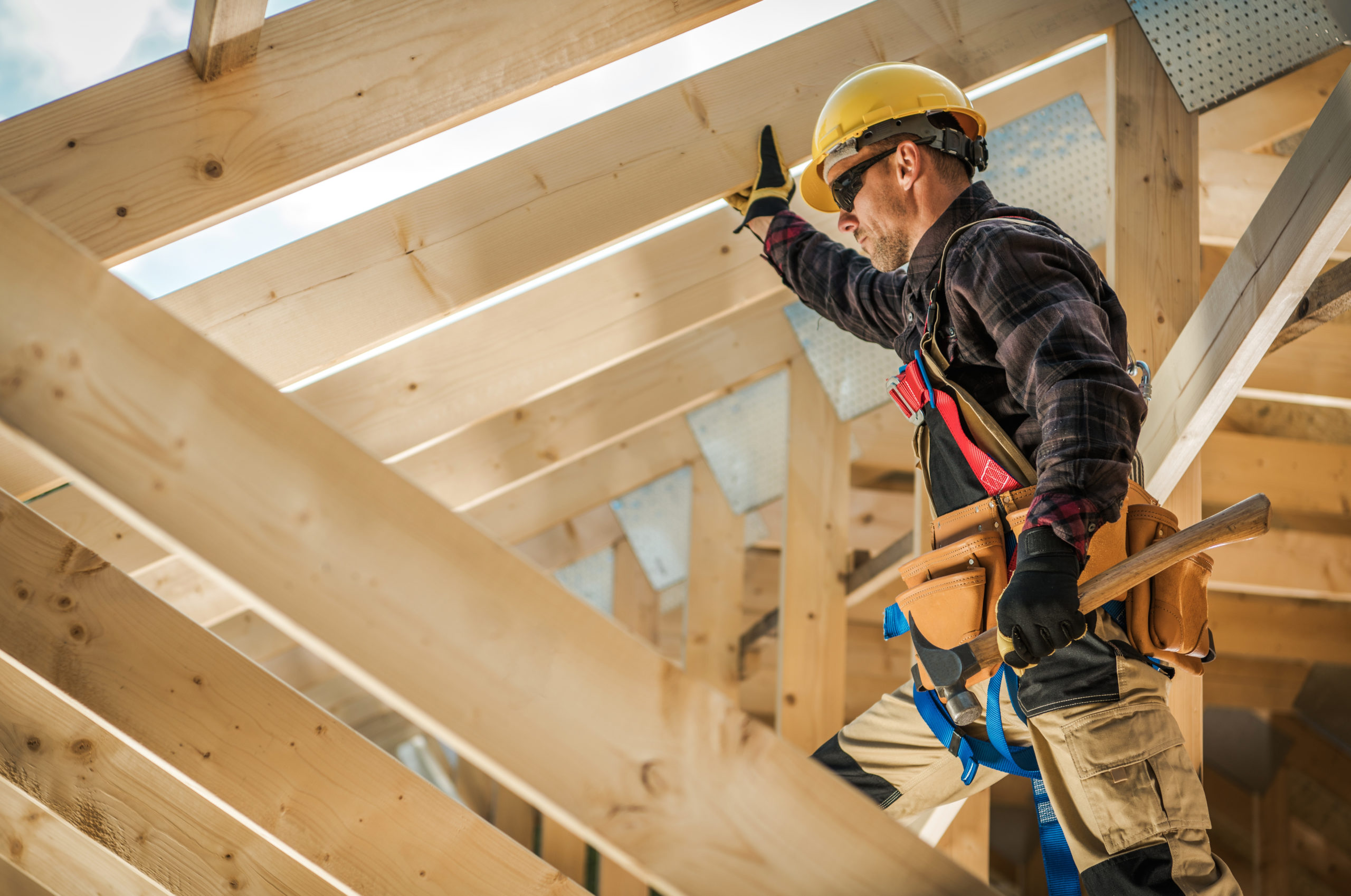 A construction worker on duty at a wooden house construction site. The worker is likely wearing safety gear such as a hard hat and reflective vest