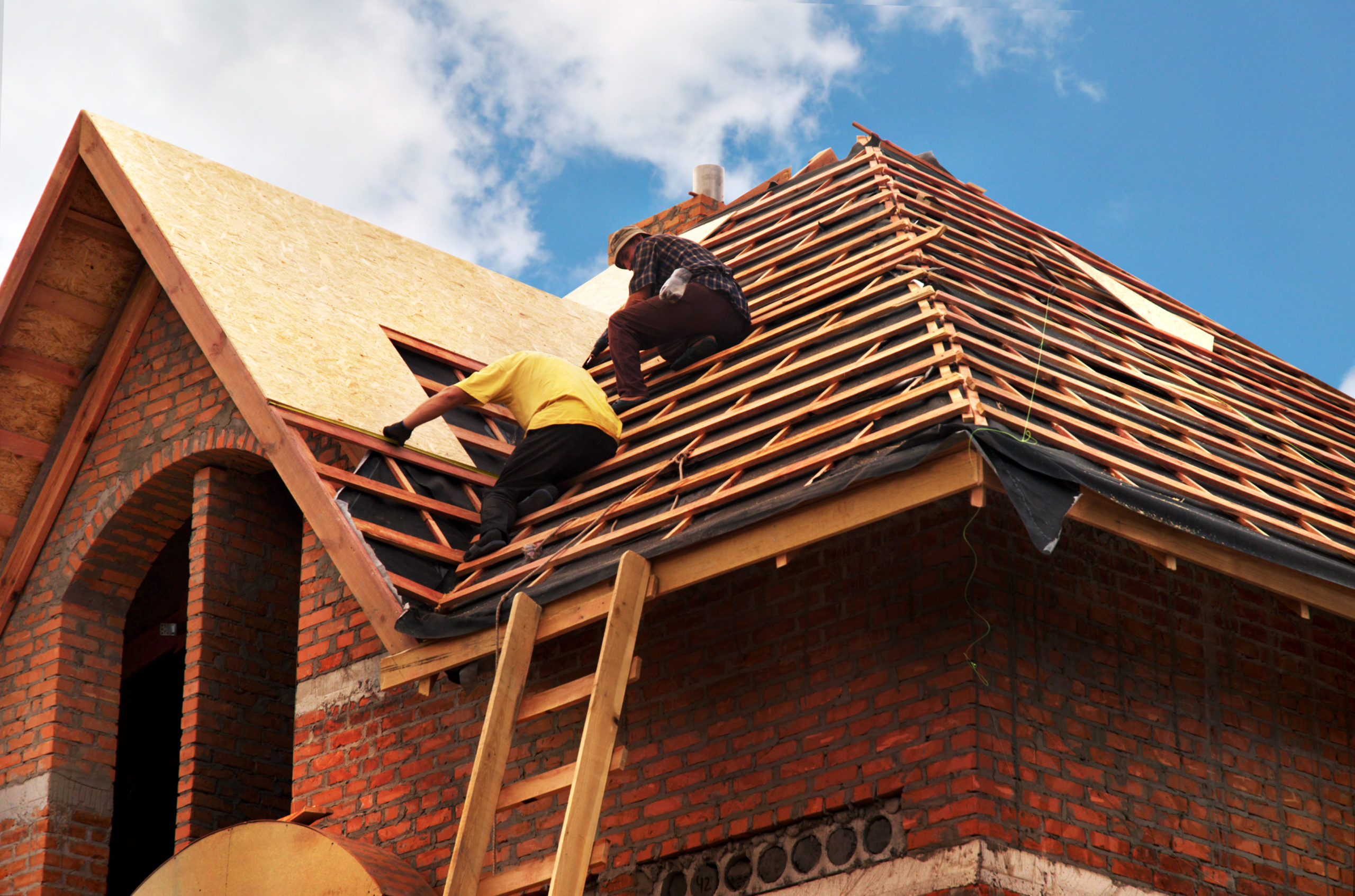 Roofing contractors installing house roof boards. The image likely shows workers on a roof, laying down boards as part of the roofing installation process